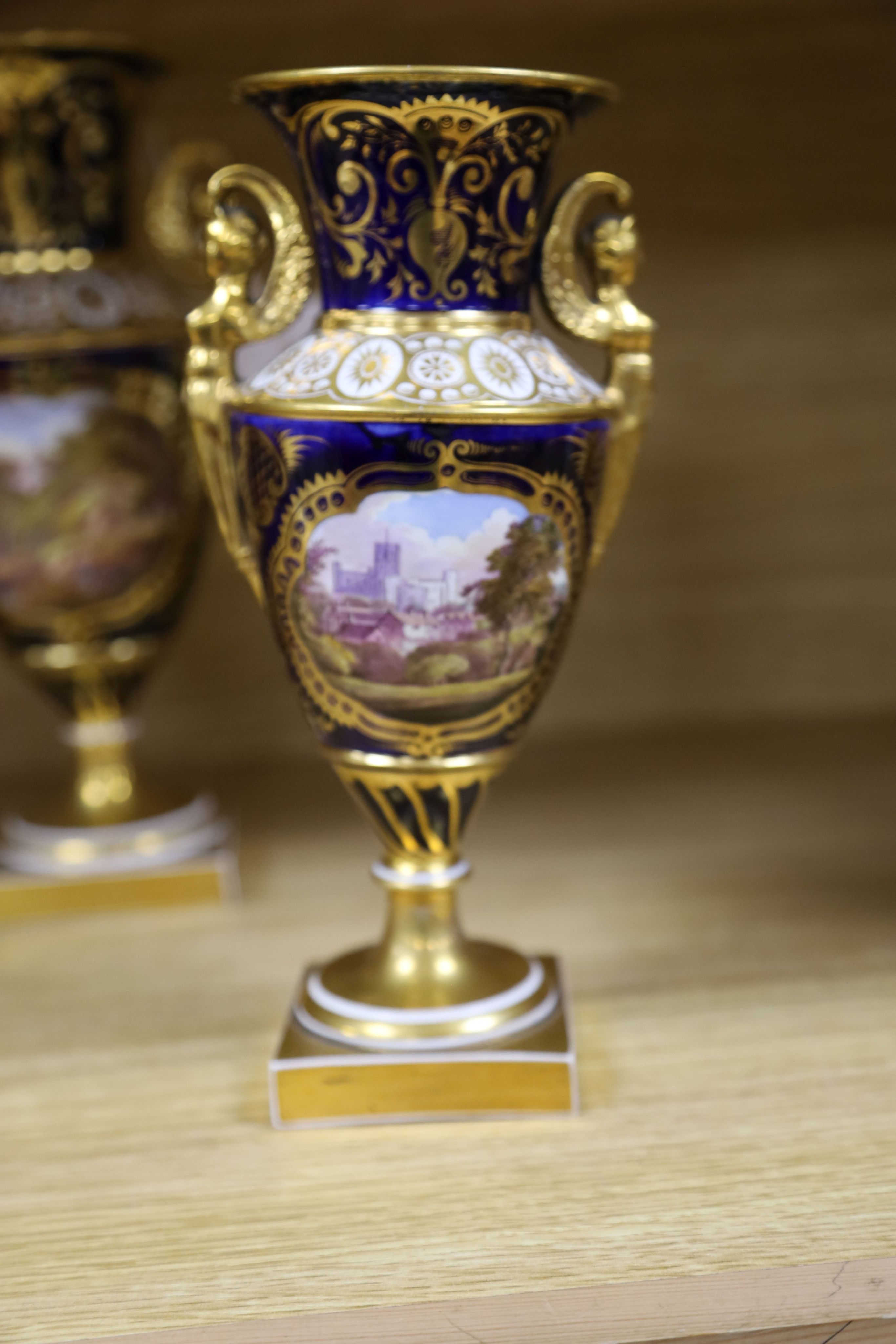 A garniture of three early 19th century English porcelain vases, c.1815-20, each painted with topographical views, tallest 26cm